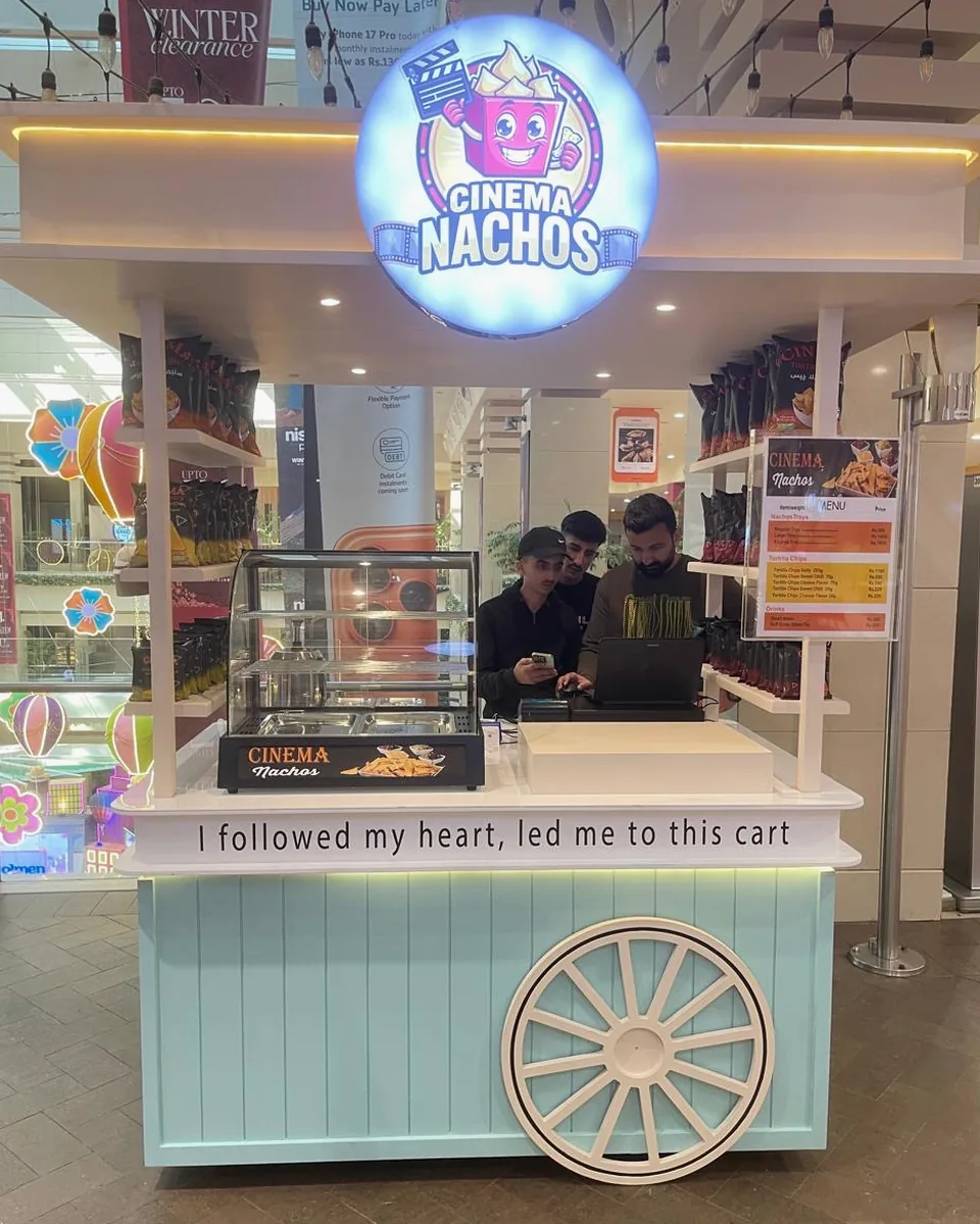 Front view of the Cinema Nachos cart at Dolmen Mall Clifton: the lit round Cinema Nachos sign above the counter, shelves of Cinema Tortilla Chips on both sides, the warm display case, the menu board and staff serving behind the counter